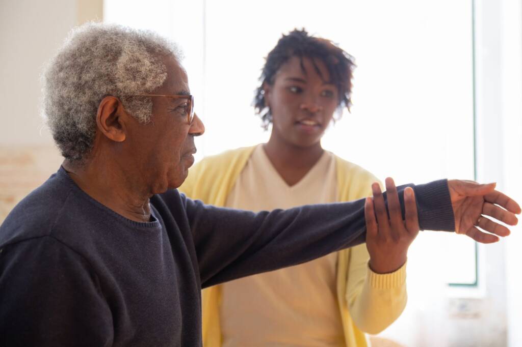 A carer helping an older man with an arm exercise at home