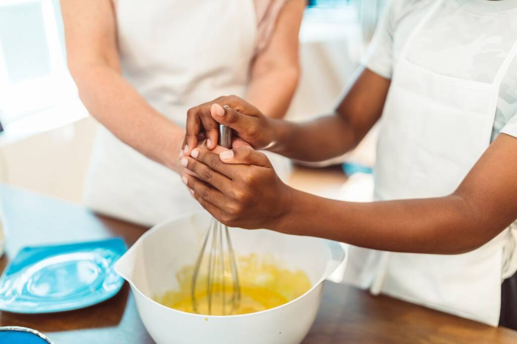 One person's hands guiding another's as they whisk batter in a bowl