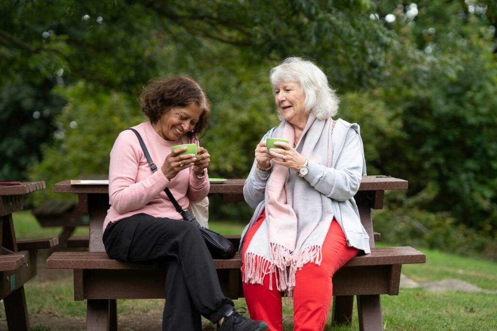Two women sharing a hot drink on a park bench