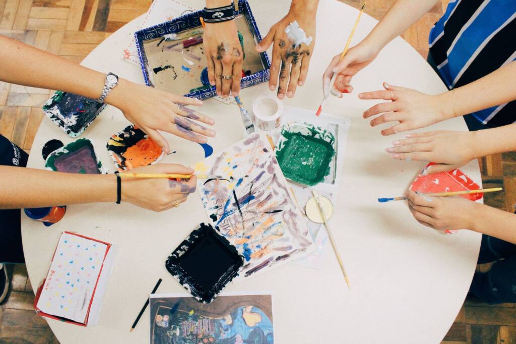Young people's hands painting together around a table, seen from above
