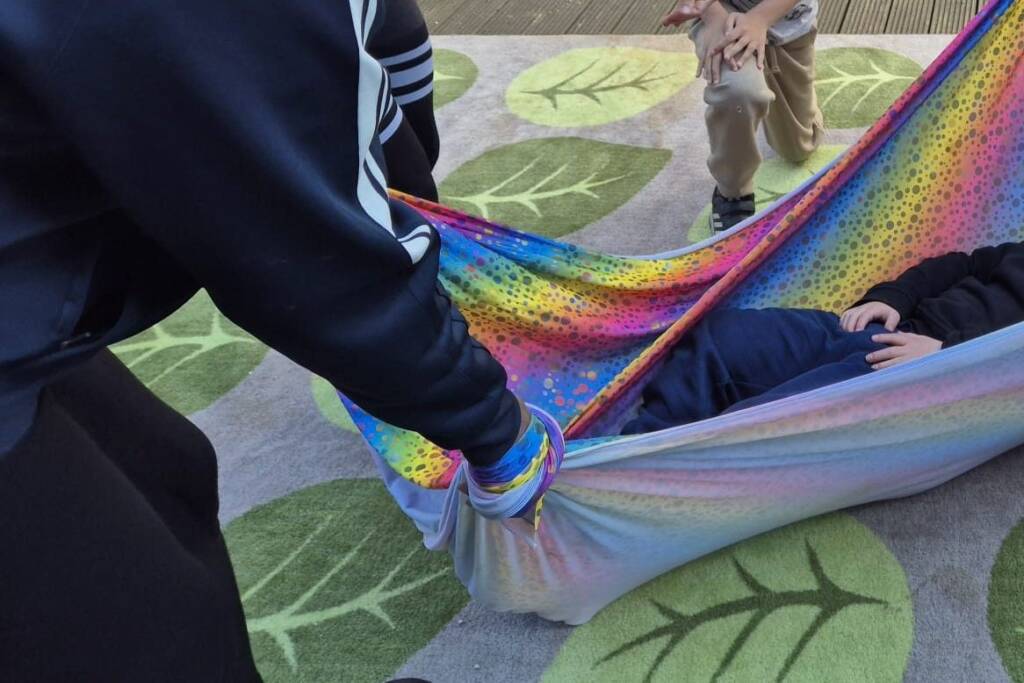 A YPEP support worker gently rocking a child in a rainbow hammock