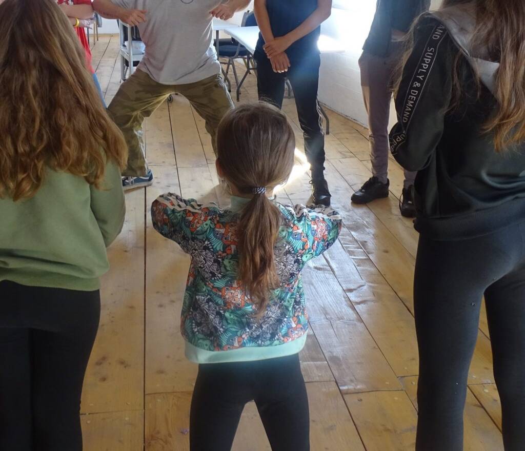 Children copying a leader’s moves in a circle, seen from behind