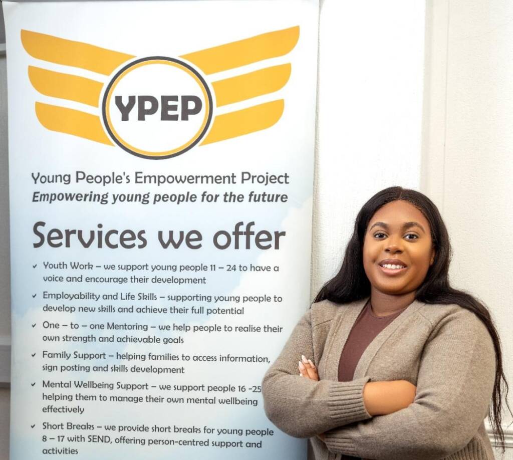 A member of YPEP's team beside a YPEP banner that reads “Empowering young people for the future”