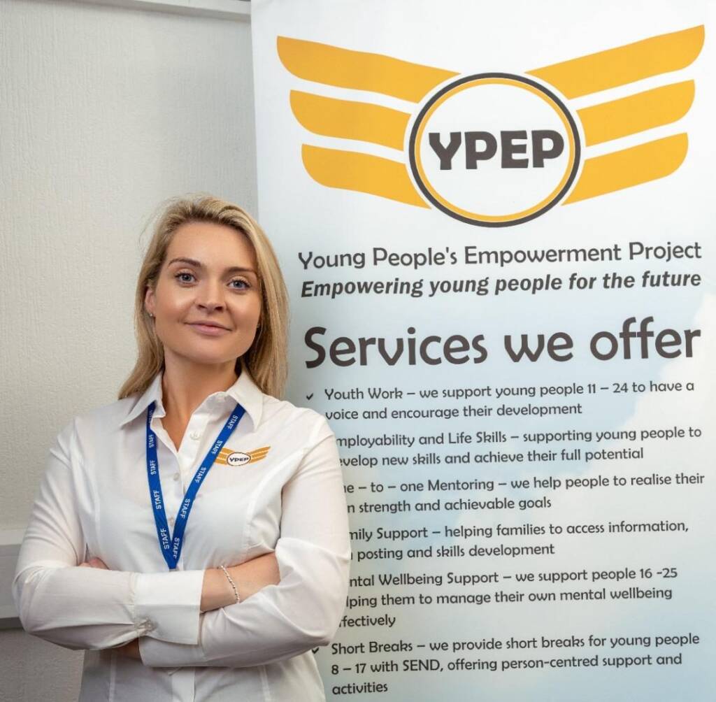 A YPEP staff member in a YPEP shirt and staff lanyard beside a YPEP banner